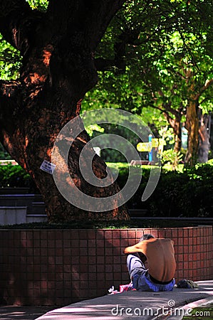 An Asian elderly sits on a bench crunch himself in a park in Hong Kong with dramatic light spot Editorial Stock Photo