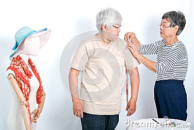 Asian elderly tailor woman show action of body measurement for the other elderly customer near cloth puppet. Image is isolated on Stock Photo