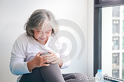 Asian elderly woman exercising at home Injured in the right knee There is a lot of pain. Stock Photo