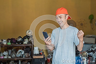 Asian electronics repairman with an excited gesture when looks at the smartphone screen Stock Photo