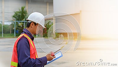 Asian engineer in safety uniform and white helmet holding walkie-talkie and clipboard on blurred industry plant background Stock Photo