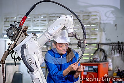 Asian factory worker woman hold tablet and maintenance with check part of robotic machine in workplace area. Industrial and Stock Photo