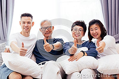 Asian family with adult children and senior parents giving thumbs up and relaxing on a sofa at home together. Stock Photo