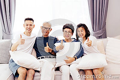 Asian family with adult children and senior parents giving thumbs up and relaxing on a sofa at home together. Stock Photo