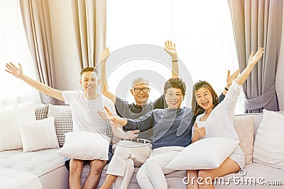 Asian family with adult children and senior parents raising hands up and sitting on a sofa at home. Happy and relaxing family time Stock Photo