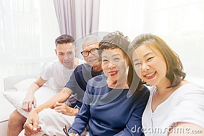 Asian family with adult children and senior parents taking selfie and sitting on a sofa at home. Happy and relaxing family time Stock Photo