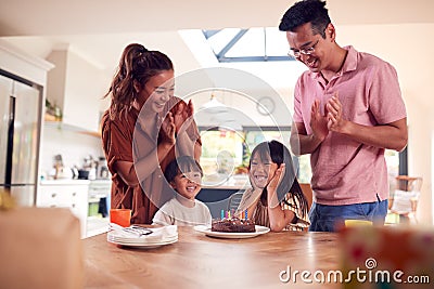 Asian Family Celebrating Daughters Birthday At Home Surprising Him With Candle Covered Cake Stock Photo