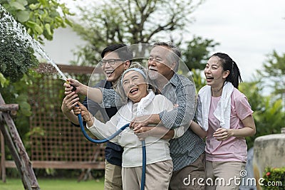 Asian family haapy with smil lovely are watering a tree by tube in garden at outdoor house in morning Stock Photo