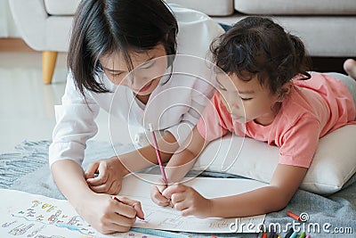 Asian family with mother and daughters are drawing on paper at home. Parents are teaching girl to draw with colors on white paper Stock Photo