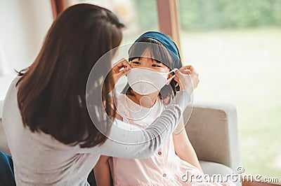 mother puts on mask for her daughter face for protection from Coronavirus Stock Photo