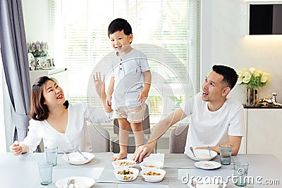 Asian family watching their kid as he is determined and proud to finally stand on the dining table. Stock Photo