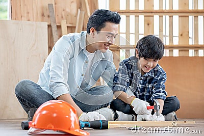 Asian father look carefully son use hammer to hopnailed in their workplace of carpentering with happy emotion. Asian family Stock Photo