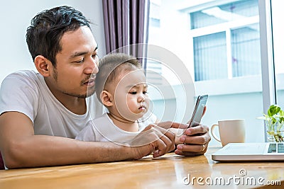 Asian father and son using smart phone together in home background. Technology and People concept. Lifestyles and Happy family th Stock Photo