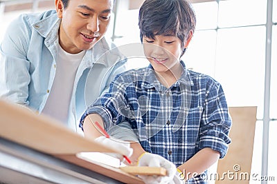 Asian father teach his son to measure and mark with pencil on wood for working with woodwork in their house. Concept of good Stock Photo