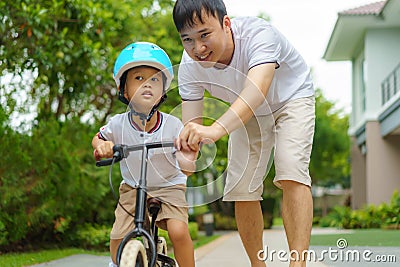 Asian father teaching his child how to ride a bicycle in a neighborhood garden, fathers interact with their children throughout Stock Photo