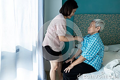 Asian female caregiver taking care of helping elderly patient get dressed,wearing clothes,button up on the shirt for happy senior Stock Photo