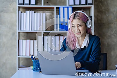 Asian female college student wearing headphones studying online using mobile smartphone app contacting laptop Stock Photo
