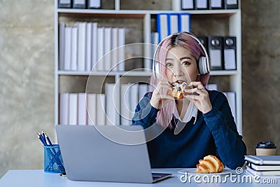 Asian female college student wearing headphones studying online using mobile smartphone app contacting laptop Stock Photo