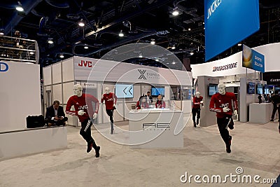 Asian female exhibitors at the AE Wireless counter surrounded by jogging JVC manequins Editorial Stock Photo