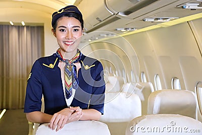 Asian female flight attendant posing with smile inside the aircraft to welcome all the passenger Stock Photo