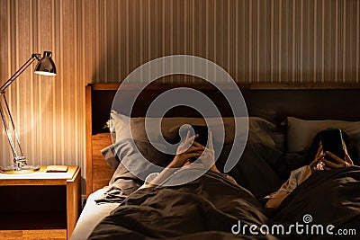 Asian female with nomophobia,excessive use of cell phone,addicted to social media,lying on bed looking at mobile phone screen in Stock Photo