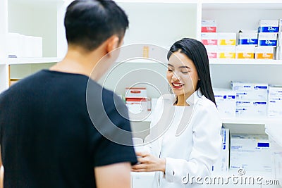 Asian female pharmacist doctor in professional gown explaining and giving advice with male client in drugstore shop. Stock Photo