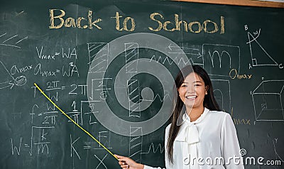 Asian female teacher smiling with wooden stick pointing to blackboard Stock Photo