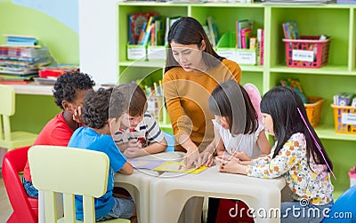 Asian female teacher teaching mixed race kids reading book in cl Stock Photo