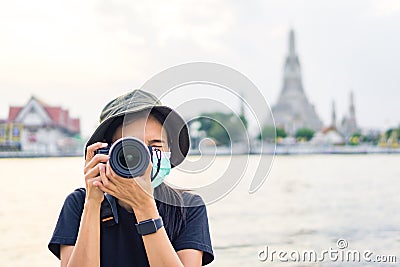 Asian female tourist wearing black shirt, wearing a hat, and taking photo, background of Wat Arun and Chao Phraya River, Bangkok, Stock Photo