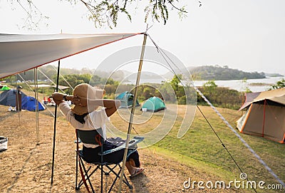 Asian female tourists sit on camping chairs, relax and have fun, camping with mountain and river views. Afternoon sunshine Stock Photo