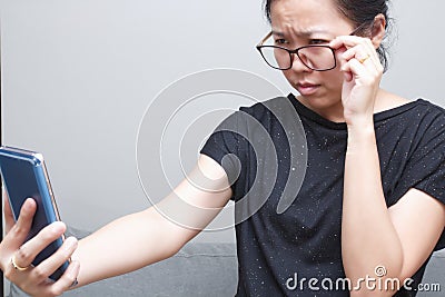 Asian female trying to read something in her mobile phone. poor sight, farsightedness, myopia Stock Photo