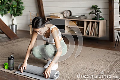 Asian fitness girl finish training,workout at home, rolling floor mat after exercising in living room Stock Photo