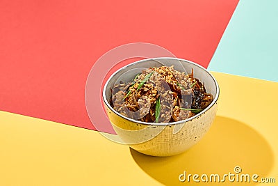 Asian fried buckwheat noodles with chicken on coloured background Fried noodles in ceramic bowl on yellow, red and blue background Stock Photo