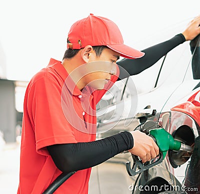 Asian gas station worker man holding green fuel nozzle into one hand and filling high energy power fuel into black auto car tank Stock Photo