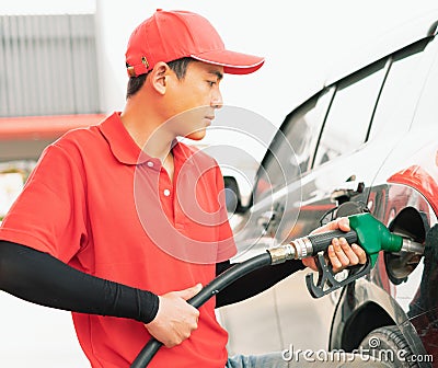 Asian gas station worker man holding green fuel nozzle with two hands and filling high energy power fuel into black auto car tank Stock Photo