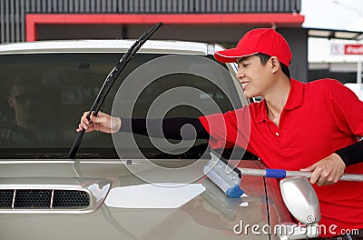 An Asian gas station worker raises the windshield wipers to clean the car windshield. A caucasian driver with sunglass raise Stock Photo