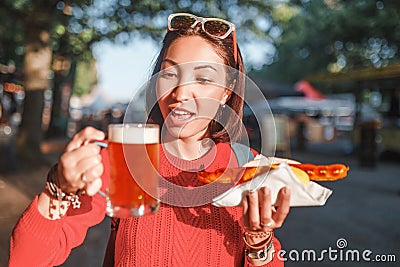 Asian girl enjoys snacking on junk food - hot dog with fried sausage and beer Stock Photo