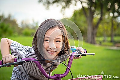 Asian girl looking at camera, smiling with a cute on bicycle in the outdoor park,child exercise in nature in the morning,healthy Stock Photo