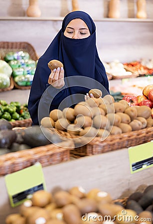Asian girl in paranja choosing kiwi in grocery Stock Photo