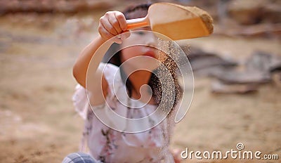 An Asian girl playing in a sandbox, sprinkling sand from a small shovel Stock Photo