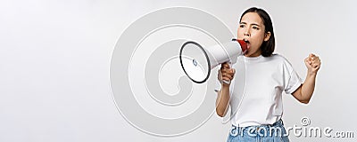 Asian girl shouting at megaphone, young activist protesting, using loud speakerphone, standing over white background Stock Photo