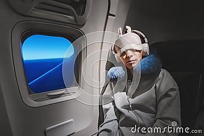 girl sleeping in her seat on the plane near the window in a mask and with a pillow to sleep. The concept of travel with Stock Photo