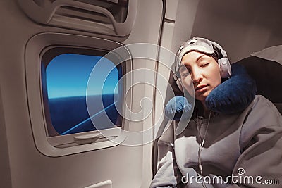 girl sleeping in her seat on the plane near the window in a mask and with a pillow to sleep. The concept of travel with Stock Photo