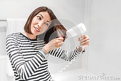 Girl smiles and dries her hair in the bathroom and looks in the mirror Stock Photo