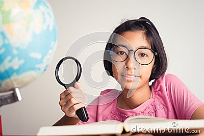 Asian girl wearing glasses is smiling and using a magnifying glass in the classroom, Educational concept Stock Photo