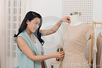 An Asian girl is working in the workshop studio. She makes fitting on the dress on the mannequin Stock Photo