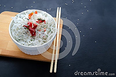 Asian glass fungoza rice noodles and bamboo sticks on a wooden board in a white round bowl with sesame seeds on a black Stock Photo