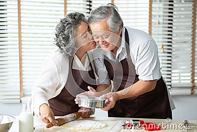 Asian Grandmother kissing Grandfather while their baking cookies Stock Photo