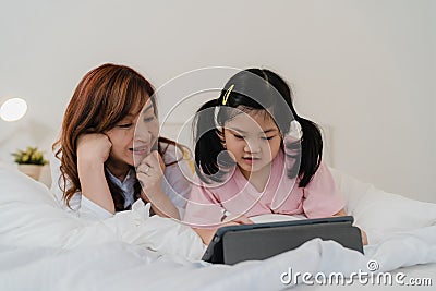 Asian grandmother using tablet read fairy tales to granddaughter at home. Senior Chinese, grandma happy relax with young girl Stock Photo