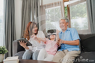 Asian grandparents and granddaughter using virtual reality and tablet play games at home. Senior Chinese, grandpa and grandma Stock Photo